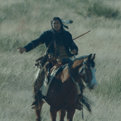 A Man Wearing A Native American Headdress Rides A Brown Horse GIF