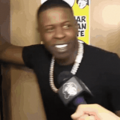A Man Wearing A Necklace And A Microphone Is Smiling . GIF
