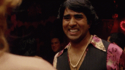 A Man Wearing A Necklace And A Pink Shirt Is Smiling At A Woman In A Club . GIF