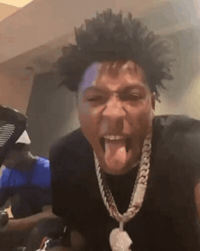 A Man Wearing A Necklace Is Sticking His Tongue Out While Making A Funny Face . GIF