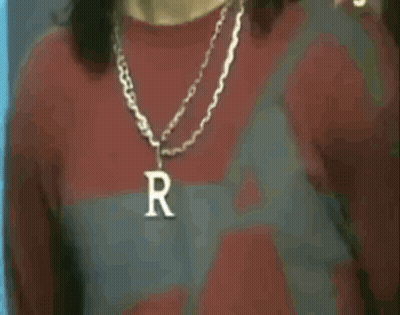 A Man Wearing A Necklace With A Letter R On It . GIF