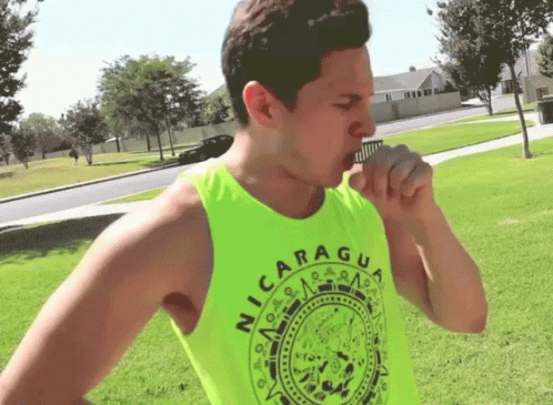 A Man Wearing A Neon Green Nicaragua Tank Top Is Coughing GIF