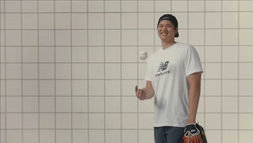 A Man Wearing A New Balance T-Shirt Laughs While Holding A Baseball GIF