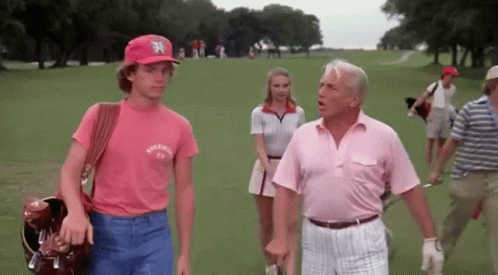 A Man Wearing A New York Yankees Hat Is Talking To A Man In A Pink Shirt GIF