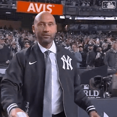 A Man Wearing A New York Yankees Jacket And Tie Is Throwing A Baseball In Front Of A Crowd . GIF