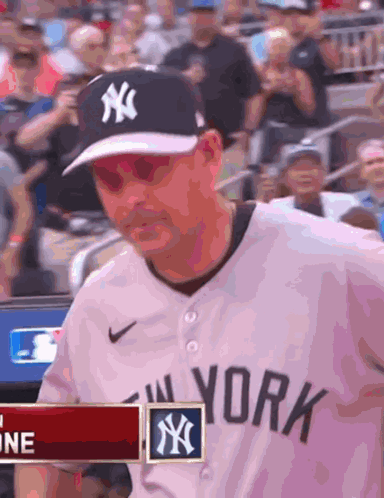 A Man Wearing A New York Yankees Jersey Is Standing In Front Of A Crowd GIF