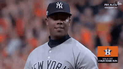 A Man Wearing A New York Yankees Jersey Stands In Front Of A Sign That Says Walk Off 2 Run Home Run GIF
