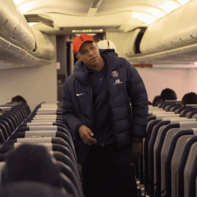 A Man Wearing A Nike Jacket Stands In An Airplane Aisle GIF