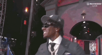 A Man Wearing A Ny Hat And Sunglasses Stands In Front Of A Screen GIF