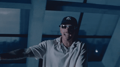 A Man Wearing A Ny Hat And Sunglasses Stands In Front Of A Window GIF