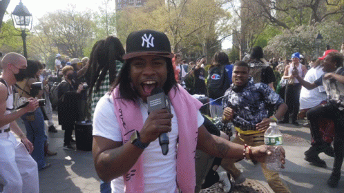 A Man Wearing A Ny Hat Is Holding A Microphone In A Crowd GIF