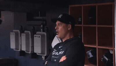 A Man Wearing A Ny Hat Stands Next To Another Man In A Black Shirt GIF