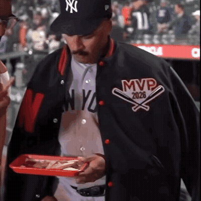 A Man Wearing A Ny Yankees Baseball Jacket Holds A Tray Of Food GIF