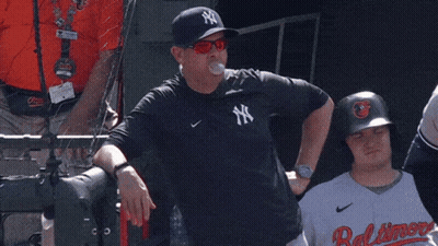 A Man Wearing A Ny Yankees Shirt Stands Next To A Baltimore Player GIF