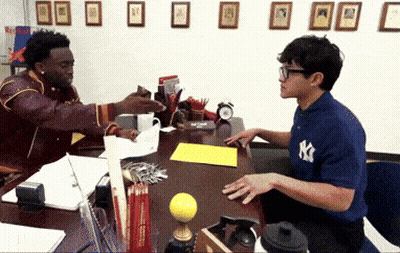 A Man Wearing A Ny Yankees Shirt Talks To Another Man At A Desk GIF