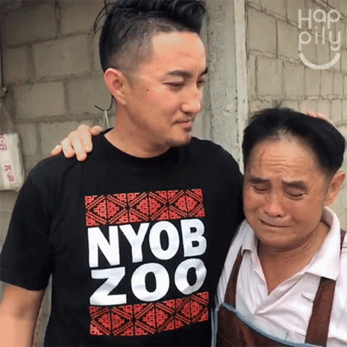 A Man Wearing A Nyob Zoo T-Shirt Hugs Another Man GIF