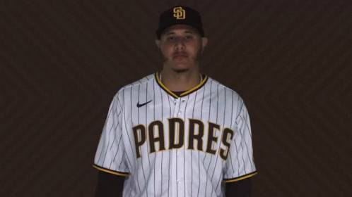A Man Wearing A Padres Baseball Jersey Stands In Front Of A Brown Background GIF