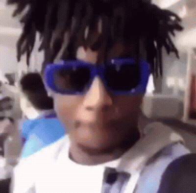 A Man Wearing A Pair Of Blue Sunglasses And Dreadlocks Is Taking A Selfie . GIF