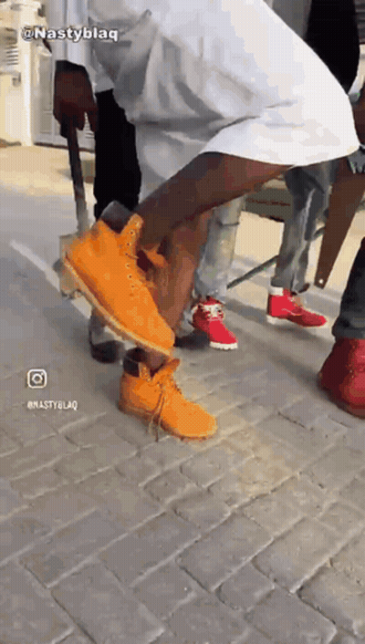 A Man Wearing A Pair Of Orange Timberland Boots Is Standing On A Brick Sidewalk GIF