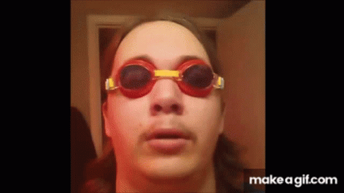 A Man Wearing A Pair Of Red And Yellow Goggles Looks At The Camera . GIF