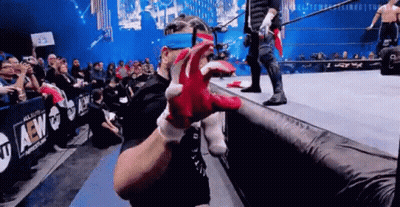 A Man Wearing A Pair Of Red Gloves Is Standing On A Wrestling Ring In Front Of A Crowd . GIF
