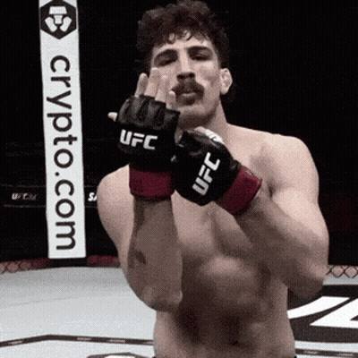 A Man Wearing A Pair Of Ufc Gloves Stands In Front Of A Crypto.com Sign GIF