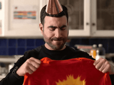 A Man Wearing A Party Hat Holds A Red Shirt GIF