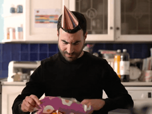 A Man Wearing A Party Hat Opens A Gift Box GIF