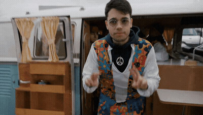 A Man Wearing A Peace Sign Necklace Is Dancing In Front Of A Van GIF