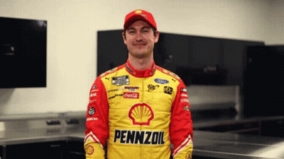A Man Wearing A Pennzoil Jacket Stands In A Room GIF
