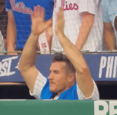 A Man Wearing A Phillies Jersey Holds His Arms Up In The Air GIF