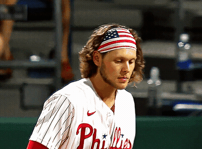A Man Wearing A Phillies Jersey With An American Flag Headband On His Head GIF