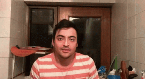 A Man Wearing A Pink And White Striped Shirt Is Standing In Front Of A Window . GIF