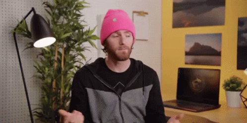 A Man Wearing A Pink Beanie Is Sitting In Front Of A Laptop Computer GIF