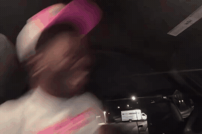 A Man Wearing A Pink Hat Is Driving A Car At Night GIF