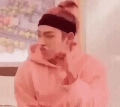 A Man Wearing A Pink Hoodie And A Headband Is Eating A Sandwich . GIF