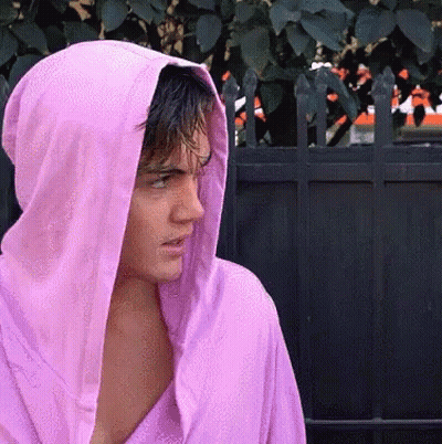 A Man Wearing A Pink Hoodie Stands In Front Of A Fence GIF