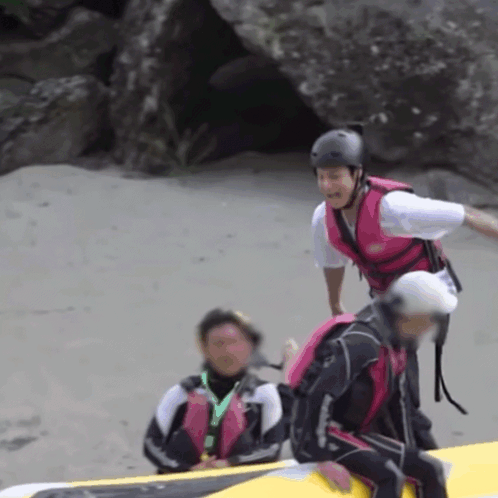 A Man Wearing A Pink Life Vest Is Standing Next To Another Man GIF