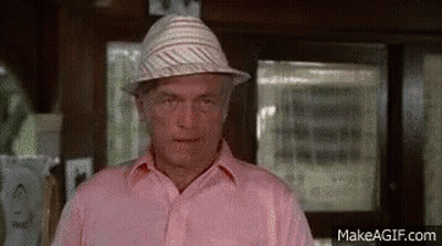A Man Wearing A Pink Shirt And A Hat Is Looking At The Camera . GIF