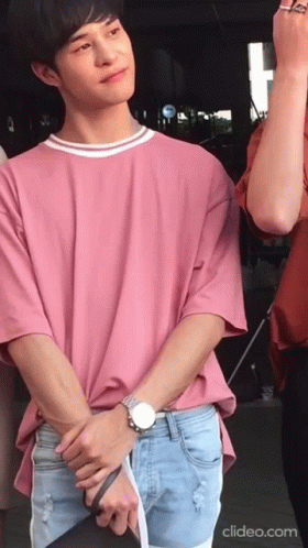 A Man Wearing A Pink Shirt And Blue Shorts Stands With His Hands Folded GIF