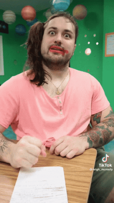 A Man Wearing A Pink Shirt Has Red Lipstick On His Lips GIF