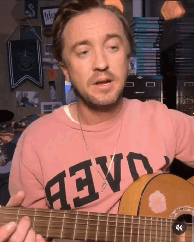 A Man Wearing A Pink Shirt That Says " Aevo " Playing A Guitar GIF