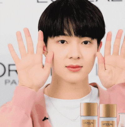 A Man Wearing A Pink Sweater Holds Up His Hands In Front Of Two Bottles Of L' Oreal Paris GIF