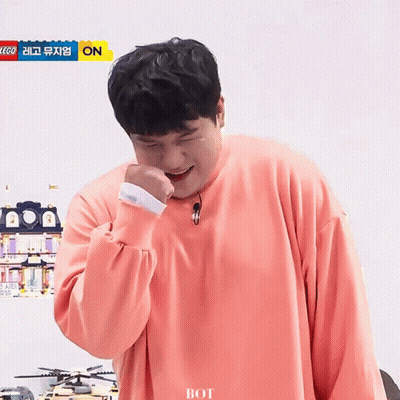A Man Wearing A Pink Sweater Is Laughing In Front Of A Sign That Says Lego On It GIF