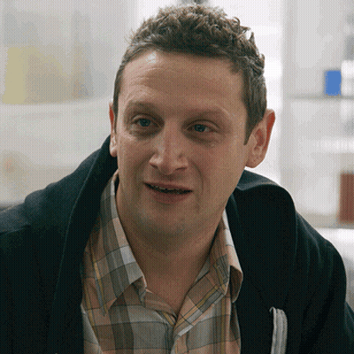 A Man Wearing A Plaid Shirt And A Black Jacket Smiles GIF