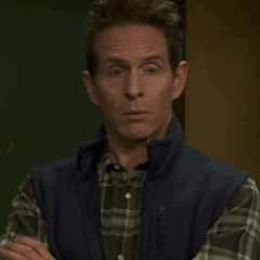 A Man Wearing A Plaid Shirt And A Blue Vest Is Looking At The Camera GIF