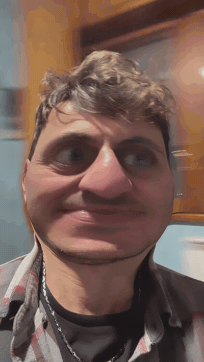 A Man Wearing A Plaid Shirt And A Necklace Makes A Funny Face GIF