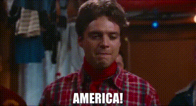 A Man Wearing A Plaid Shirt And A Red Turtleneck Is Standing In A Room And Saying `` America '' . GIF