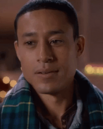 A Man Wearing A Plaid Shirt And A Scarf Is Smiling GIF