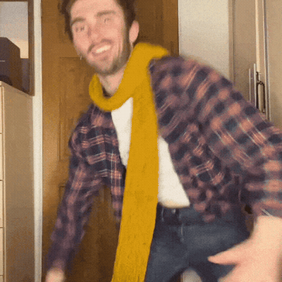 A Man Wearing A Plaid Shirt And A Yellow Scarf Dancing GIF
